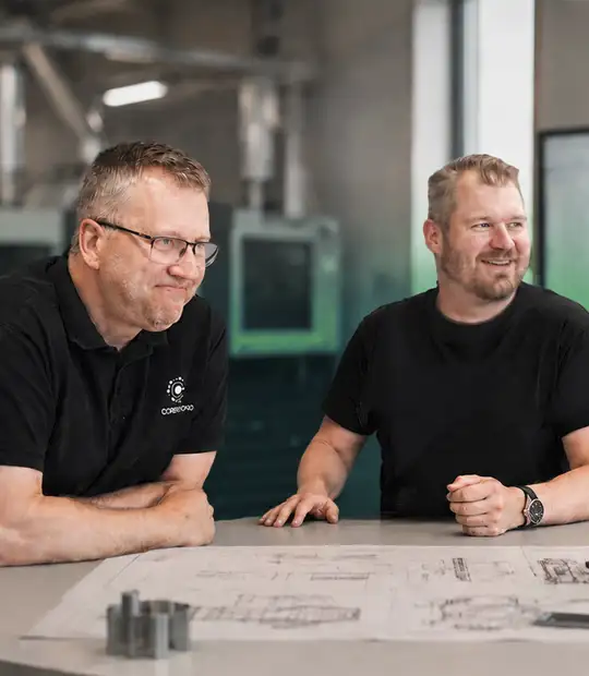 Coresbondin Mikko ja Kimmo hymyilevät suunnittelupöydän äärellä
